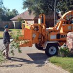 Ágdarálás A person operates a wood chipper to trim and manage tree branches outdoors.